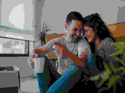 Young couple drinks coffee and cuddles surrounded by moving boxes.